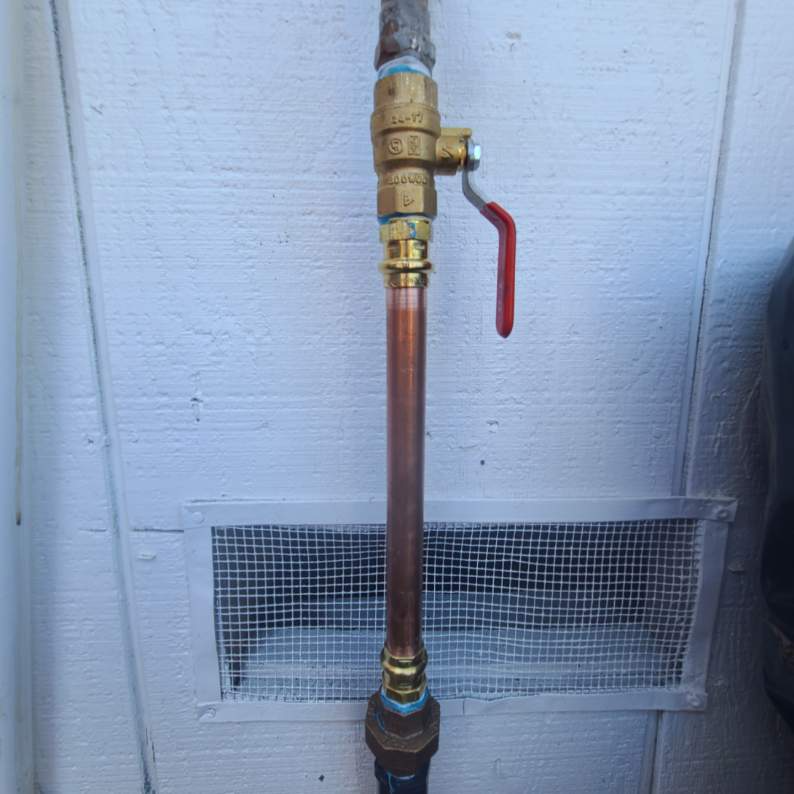 Copper pipe with a brass valve and handle attached to a gas line, mounted on a white wall.