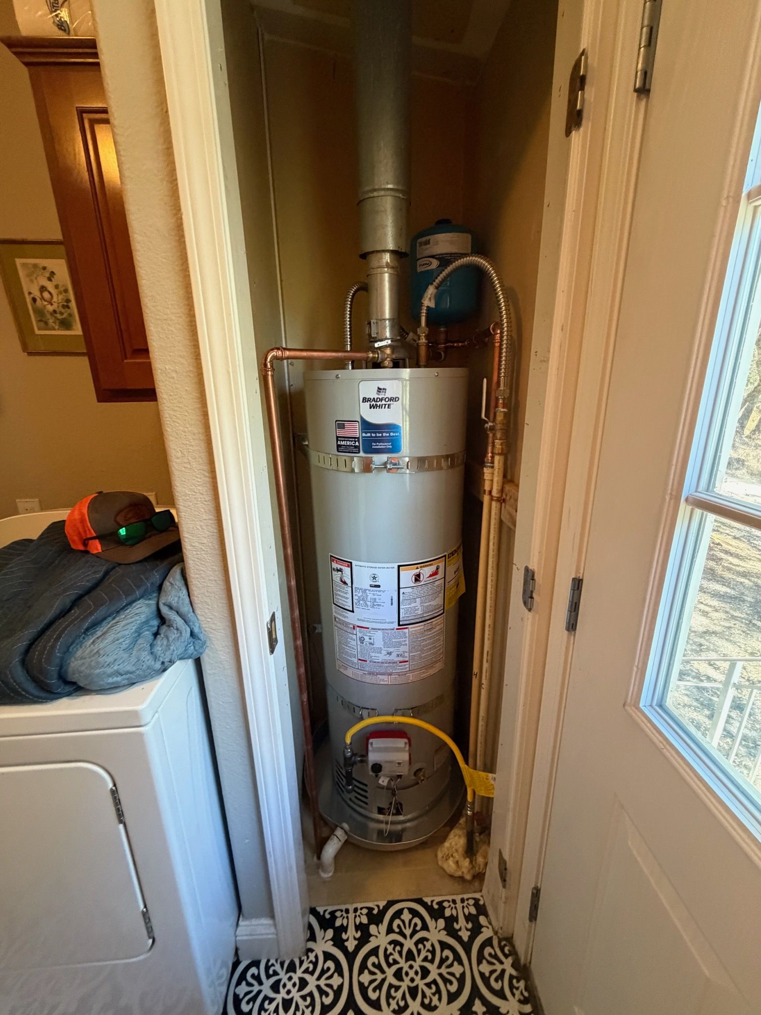Water heater in a narrow utility closet beside a laundry area and window.