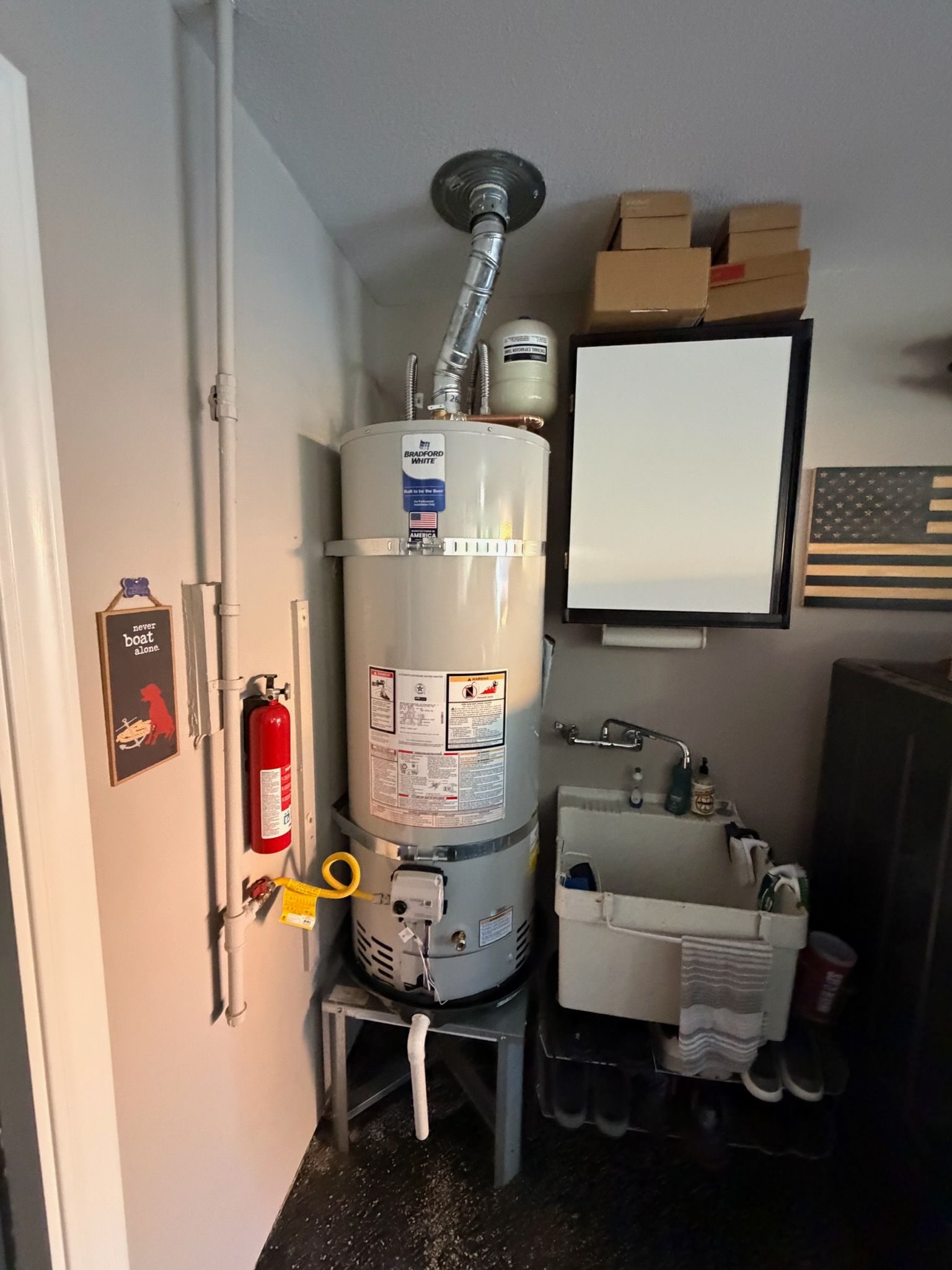 Basement utility room with a large water heater, furnace piping, sink, mirror, and fire extinguisher.