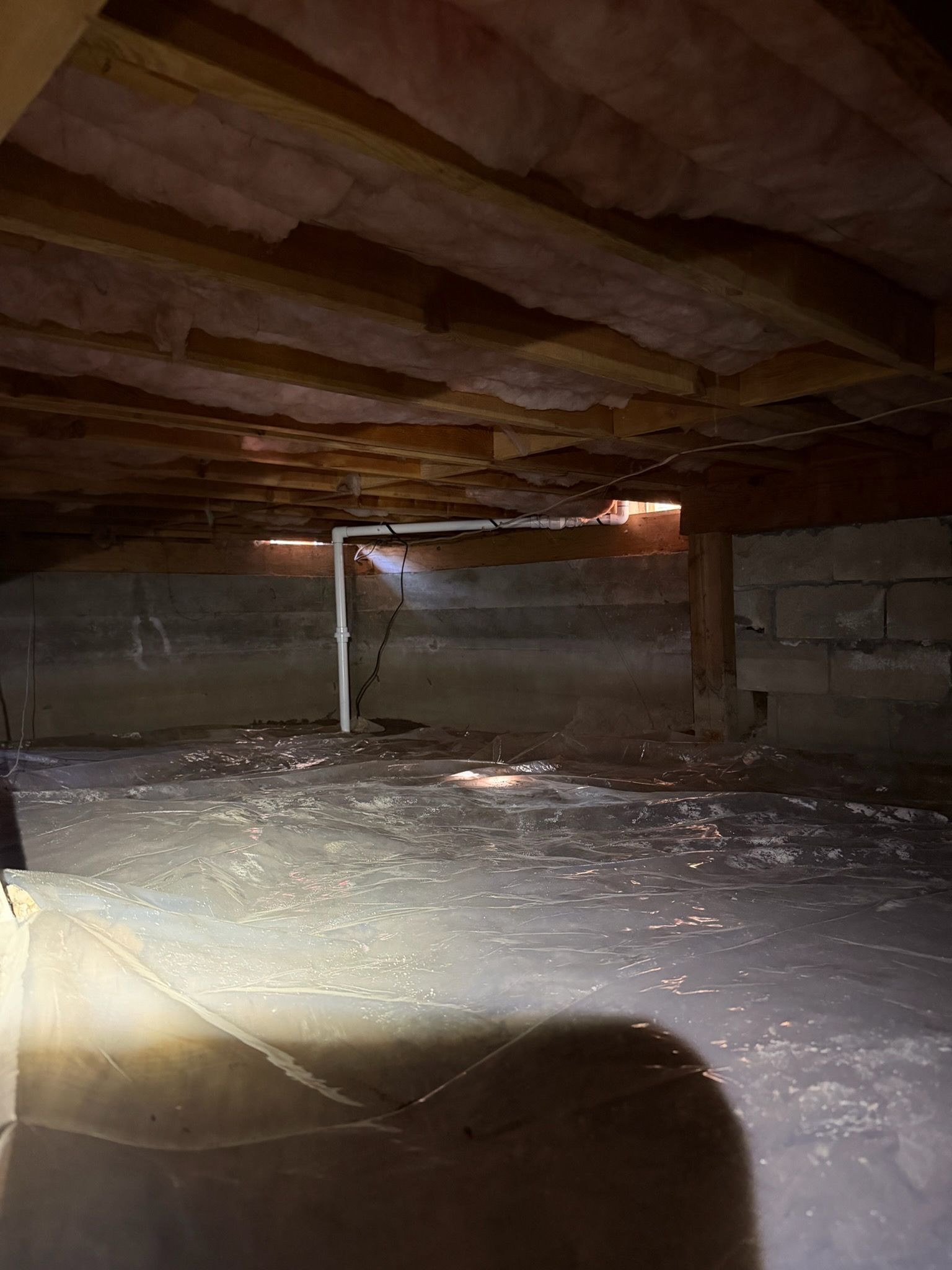 Crawlspace with exposed beams and insulation, lit by a flashlight beam across the dirt floor.