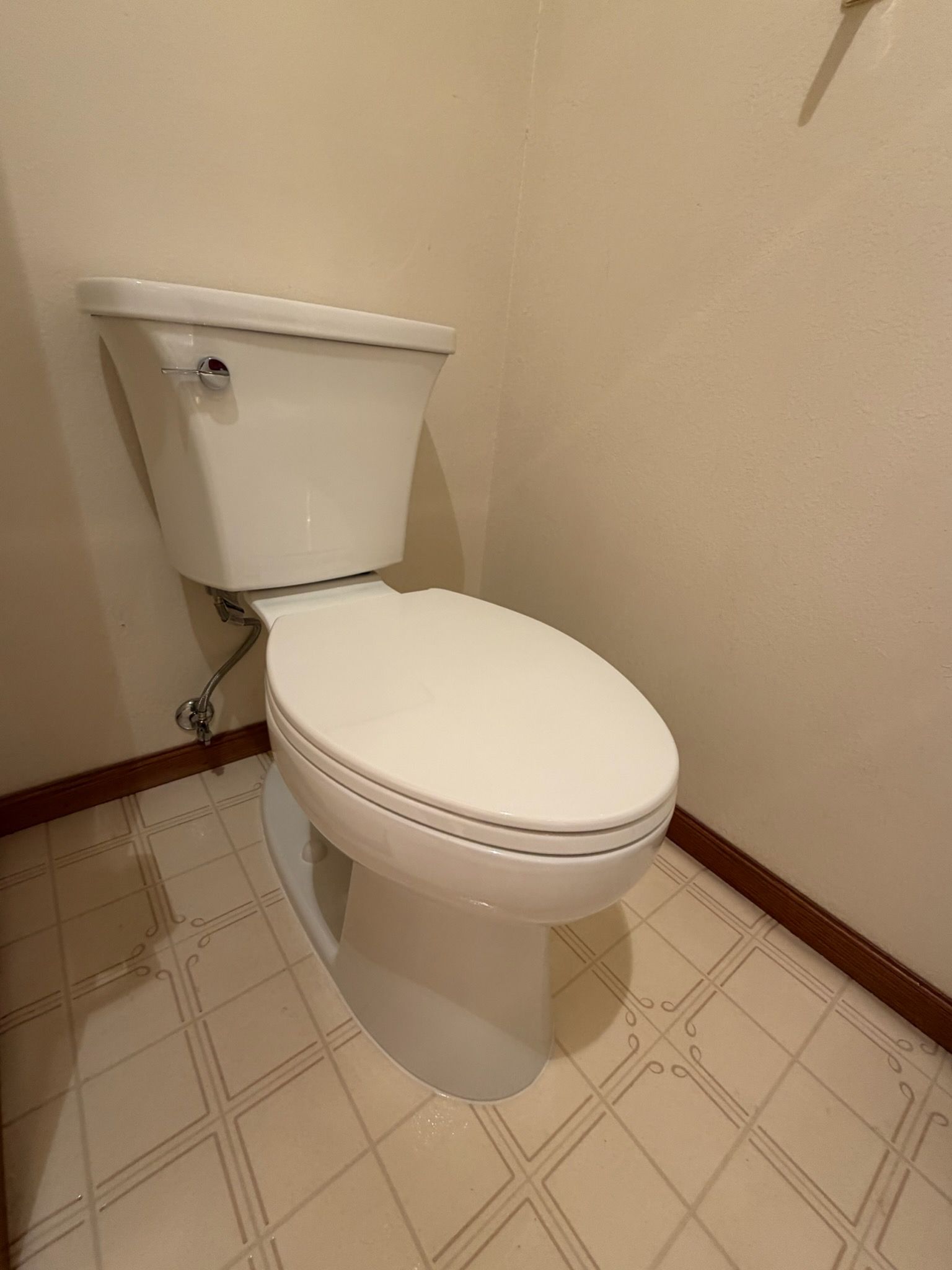 White toilet in a small beige bathroom with patterned tile floor.