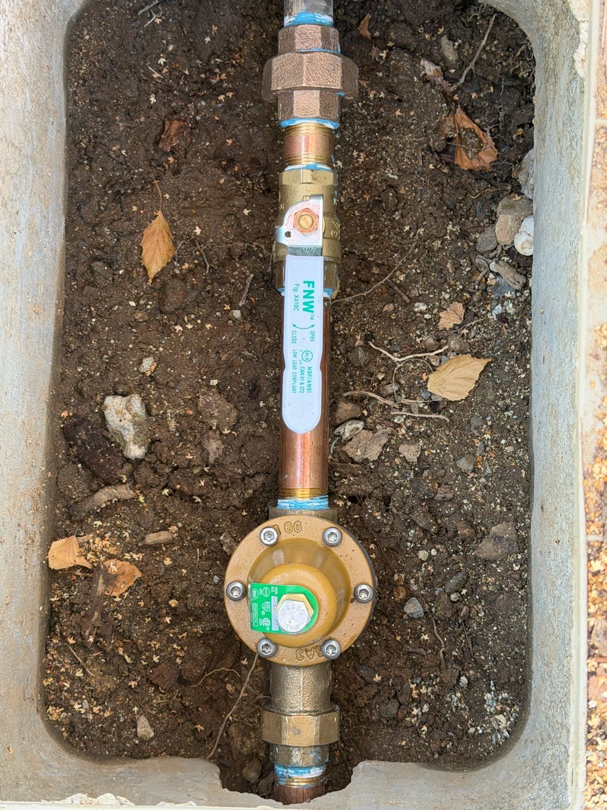 Water meter assembly in a dirt utility pit with copper piping and brass fittings.