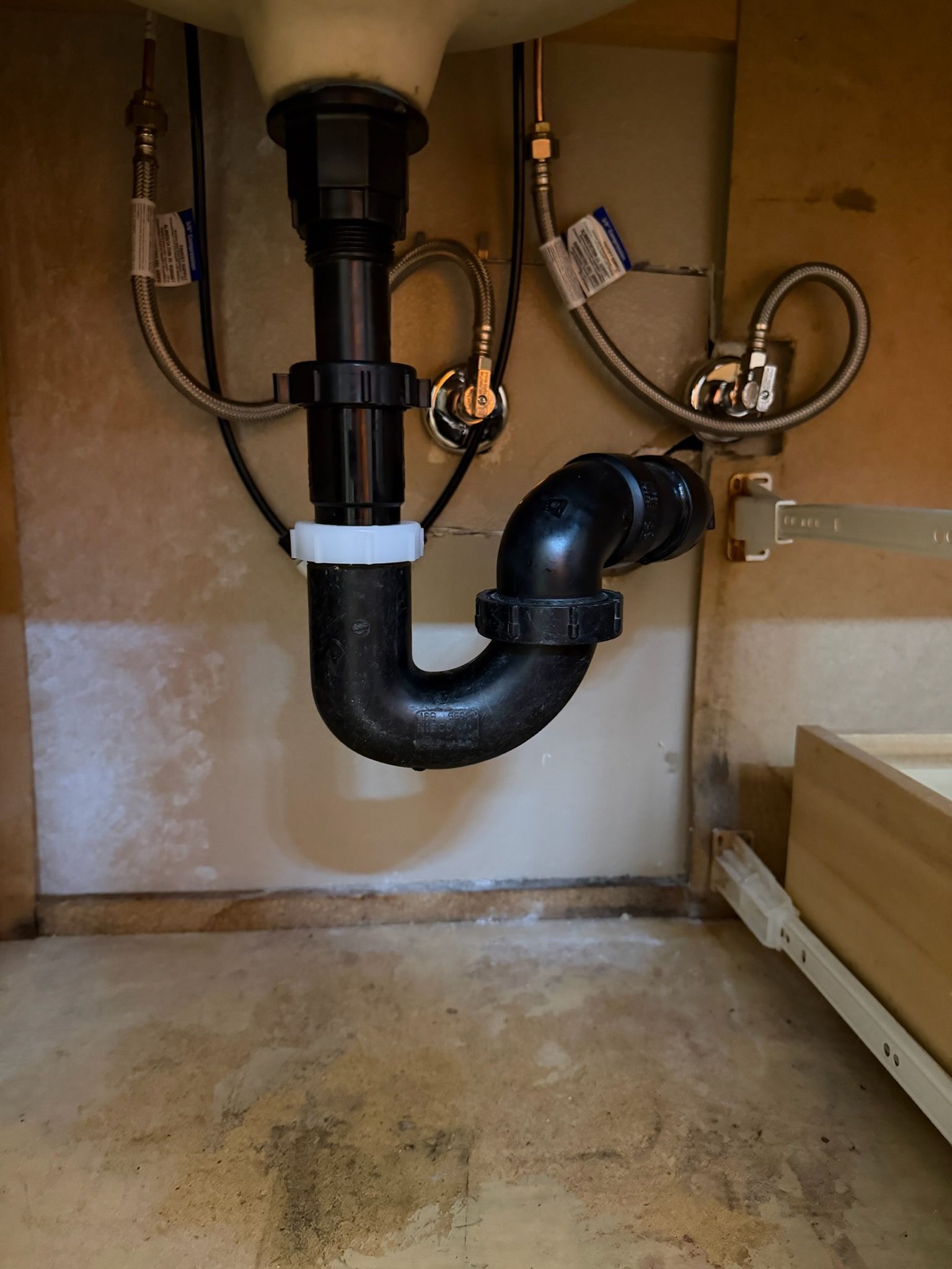 Under-sink plumbing with black drain pipes and hoses inside a cabinet
