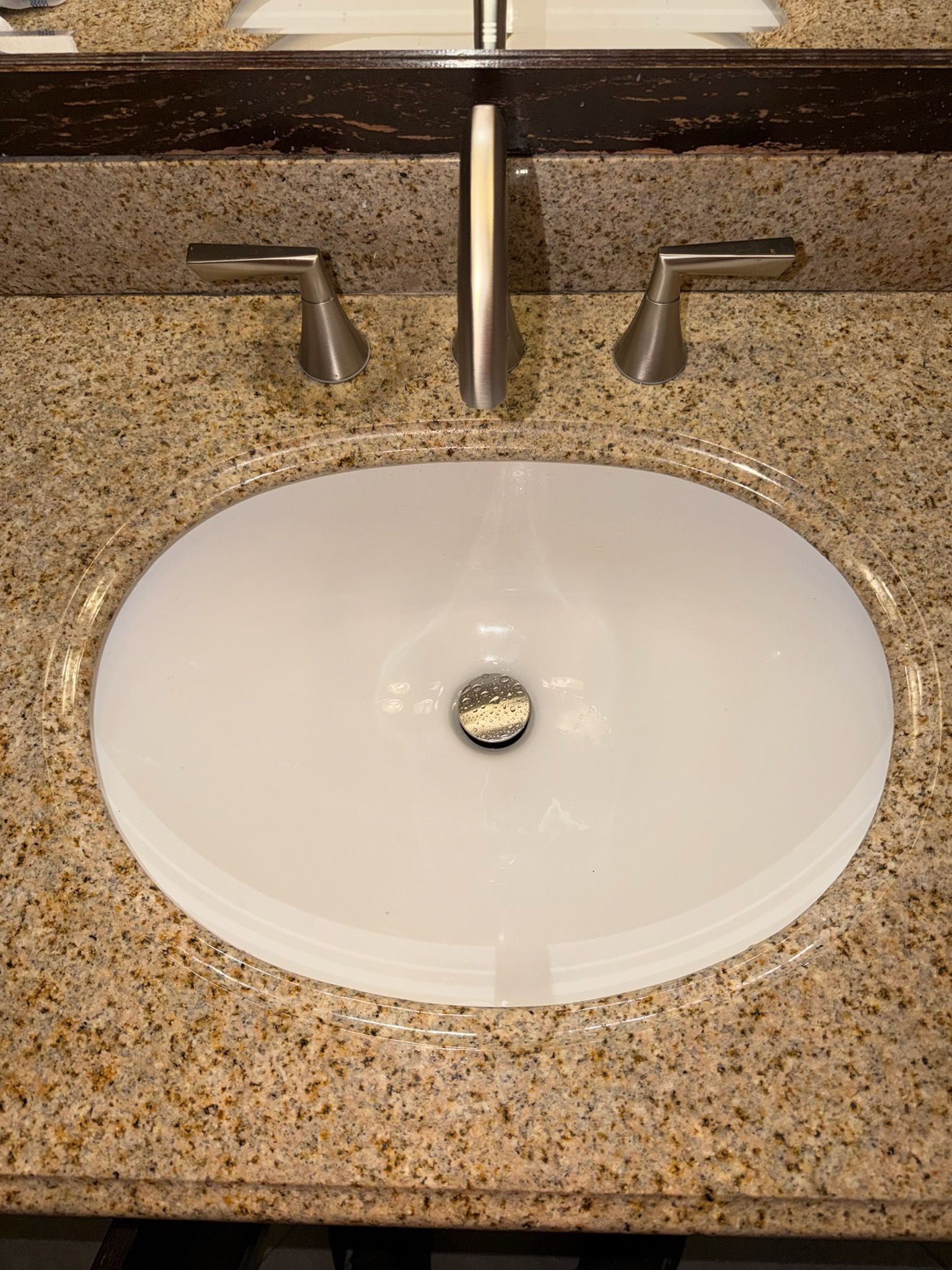 Bathroom sink with granite countertop, white oval basin, and brushed metal faucet and handles