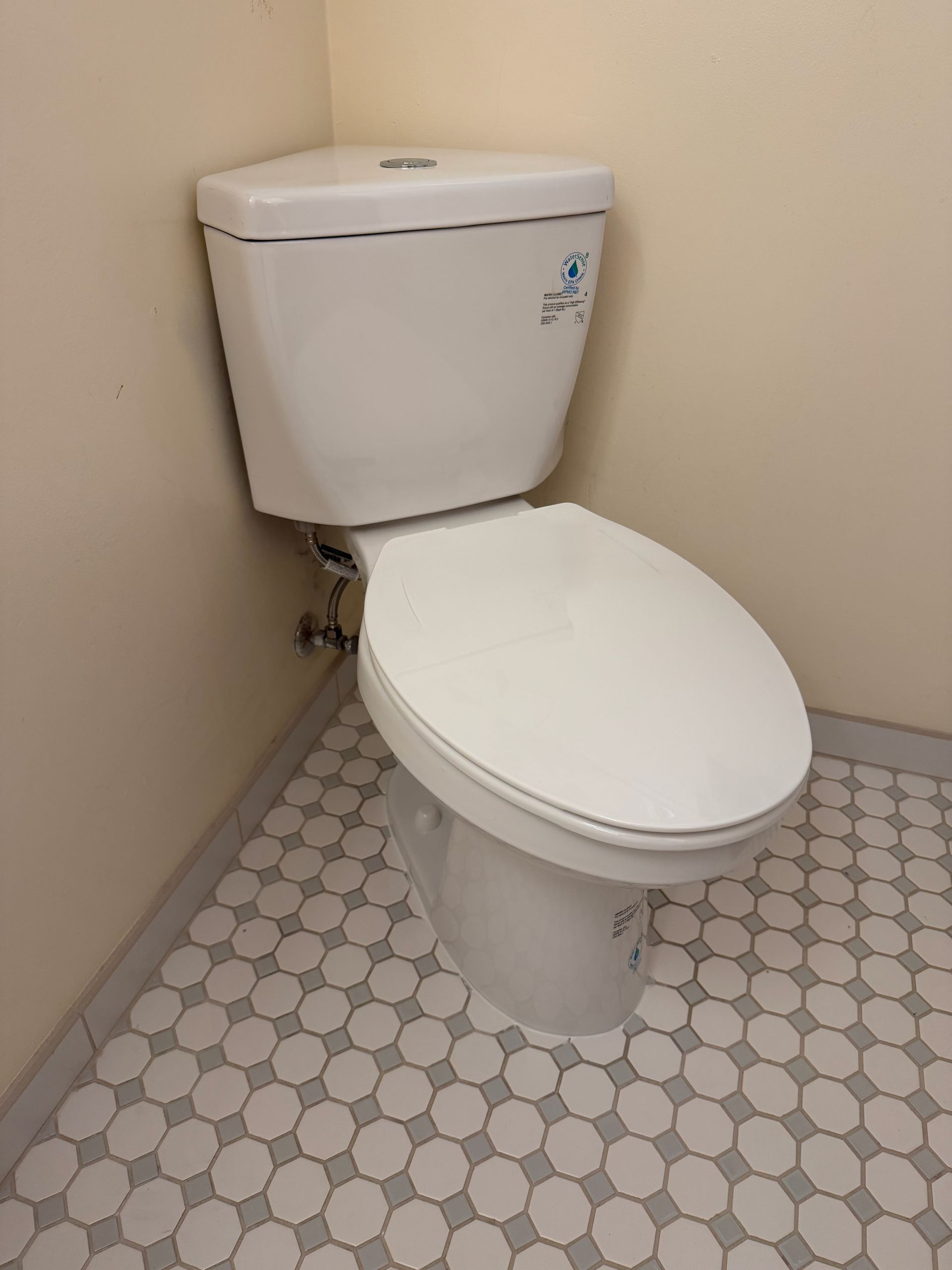 Small bathroom with a white toilet on hexagon tile floor against beige walls