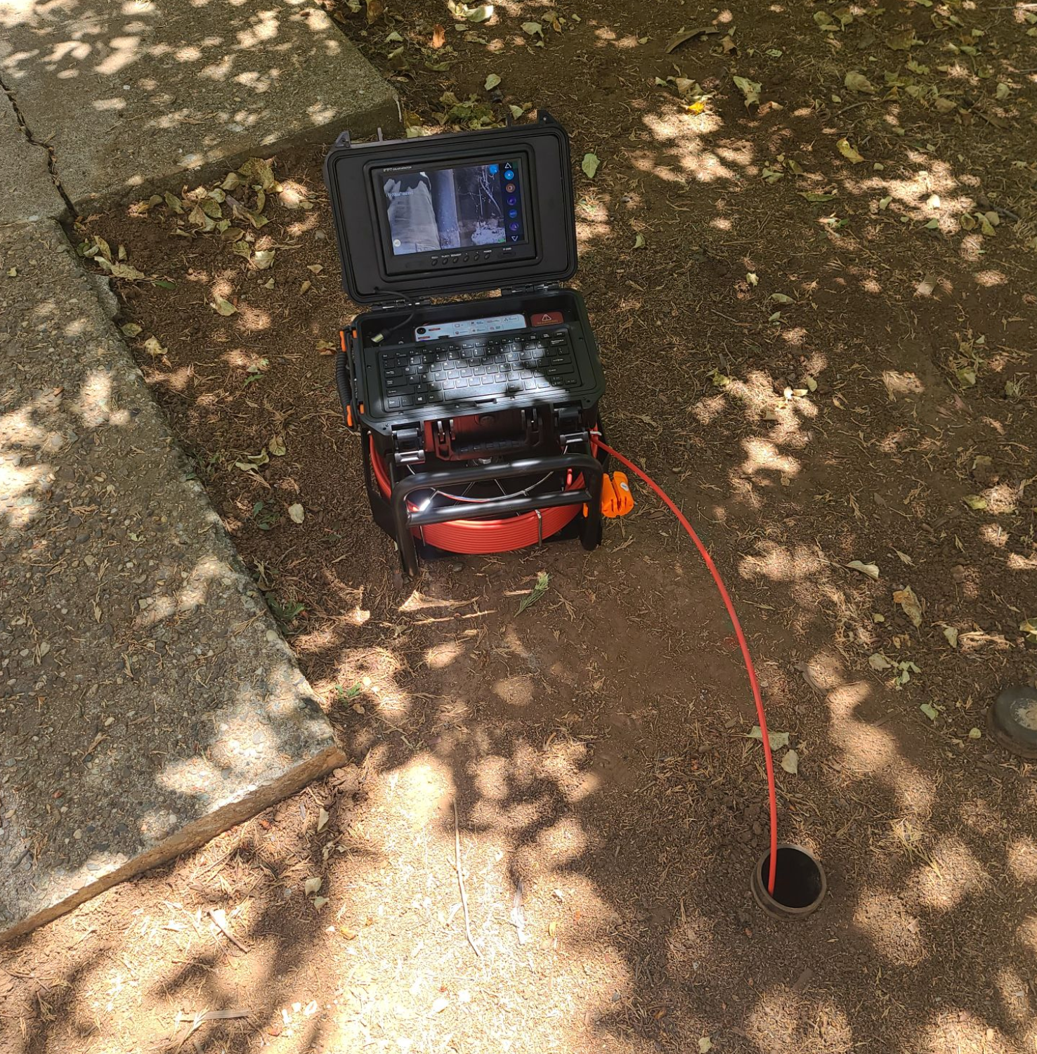A drain inspection camera next to a dark hole in the ground.