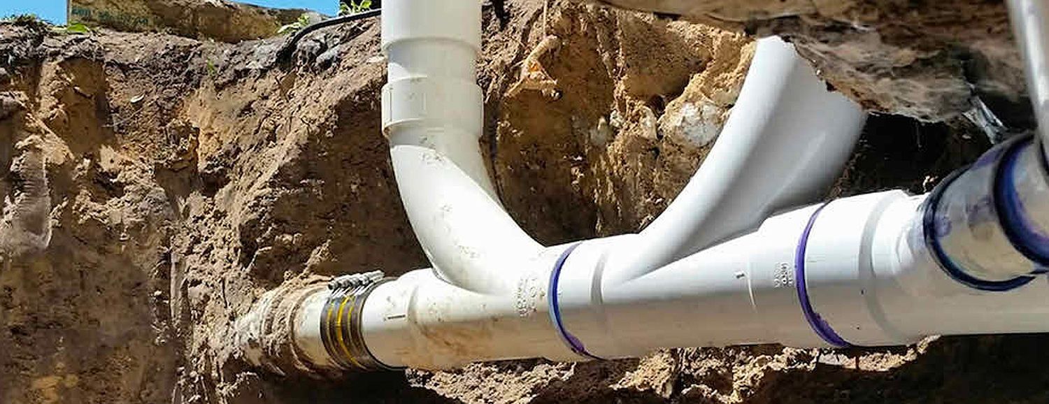 White PVC pipes with blue rings are connected and buried in brown soil.
