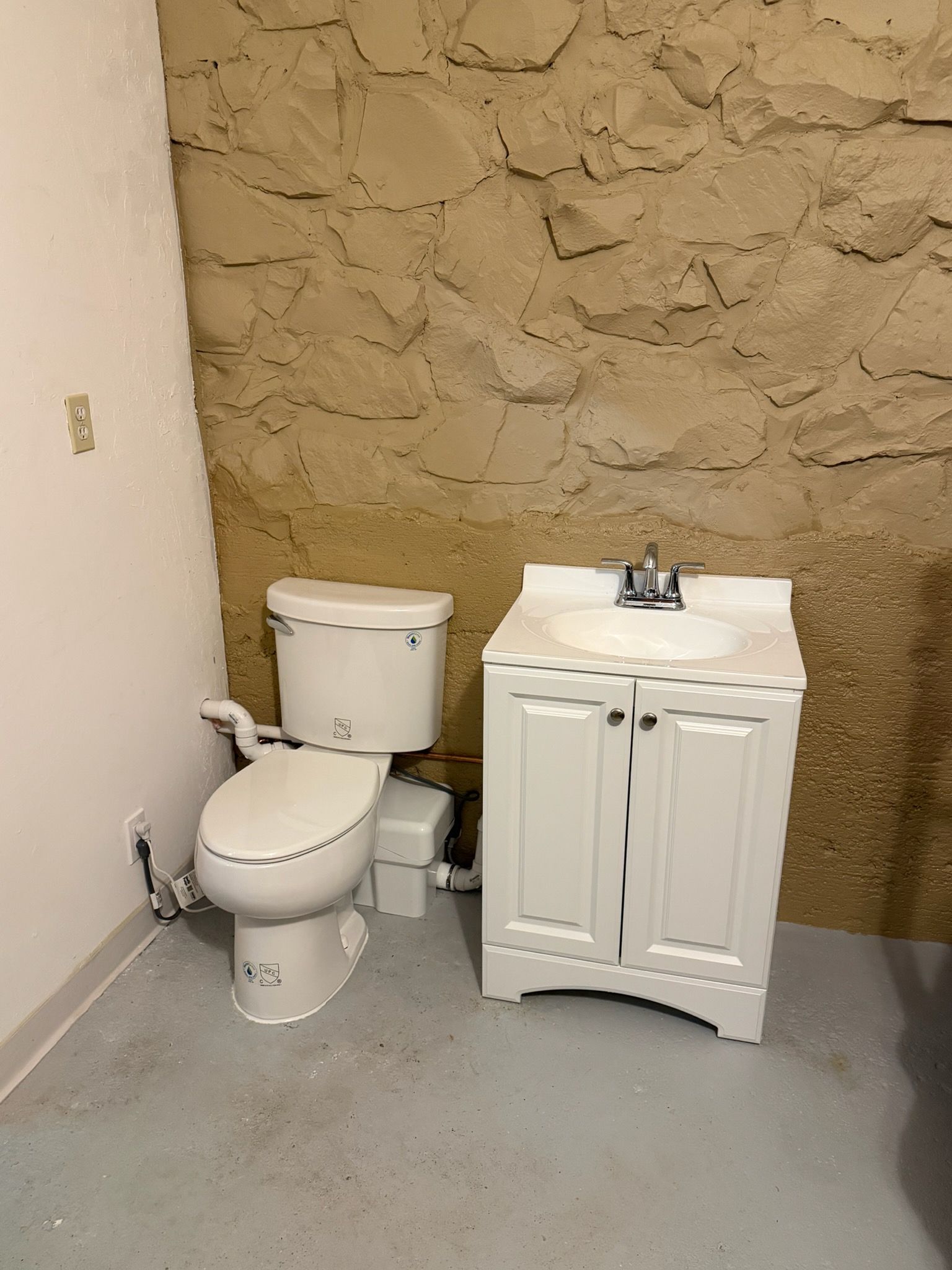 A small bathroom with a white toilet and vanity against a stone wall. Gray floor.