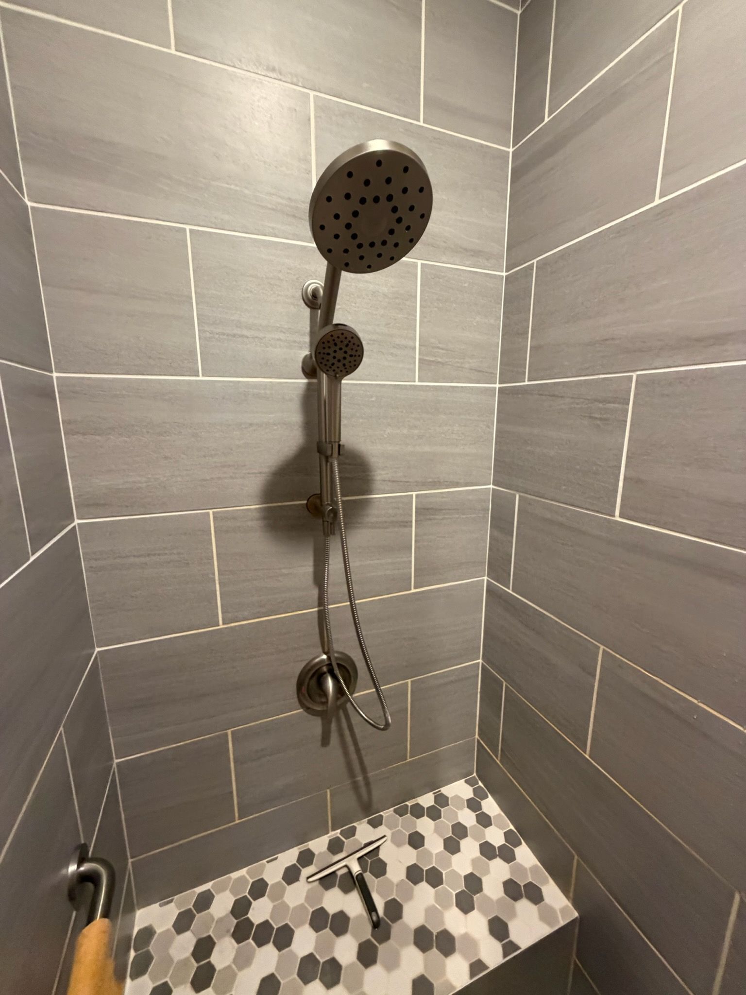 Modern tiled shower with black rain showerhead and handheld sprayer over patterned floor tiles