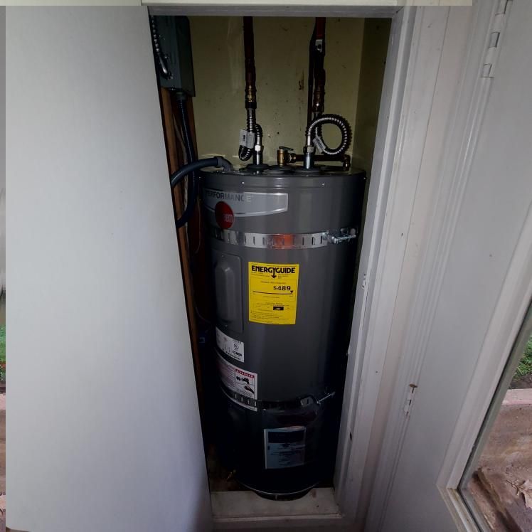 Water heater in a closet.  Gray tank with energy guide sticker. Pipes connect to the top. Closet walls are white and yellow.