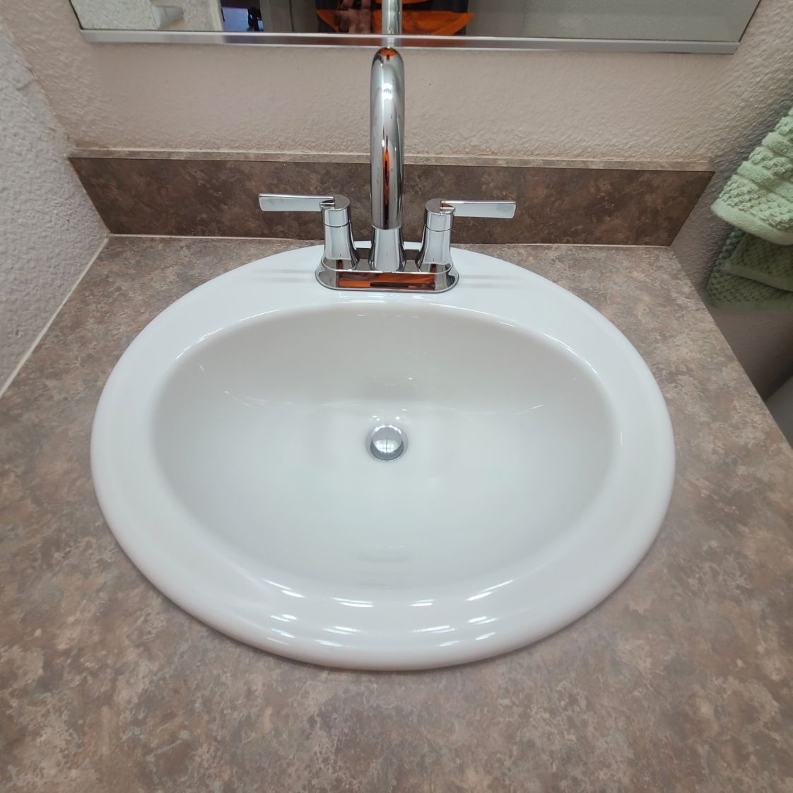 White oval bathroom sink with chrome faucet on a brown countertop.