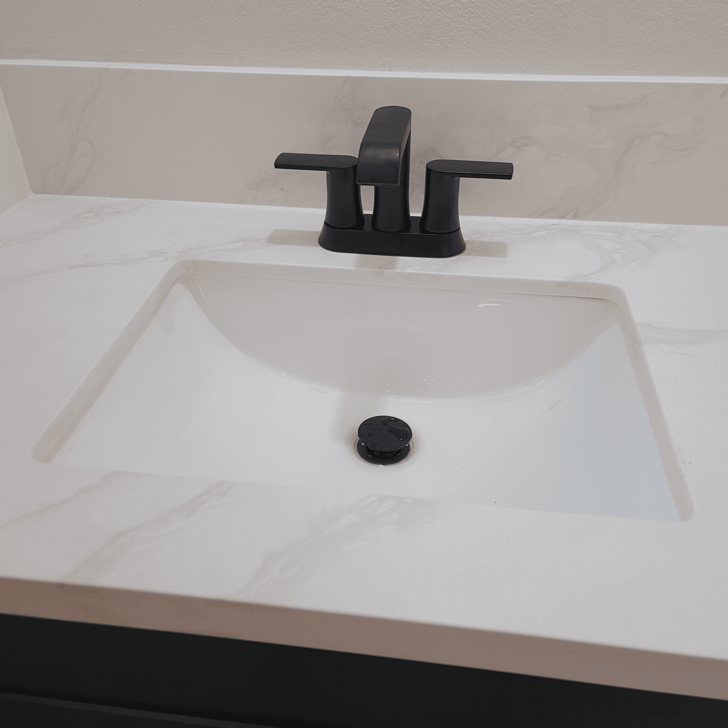 White bathroom sink with black faucet, in a vanity with a patterned countertop.