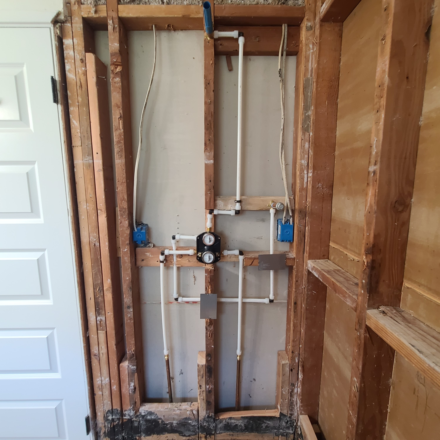 Framed wall with exposed plumbing and electrical wiring for a shower.