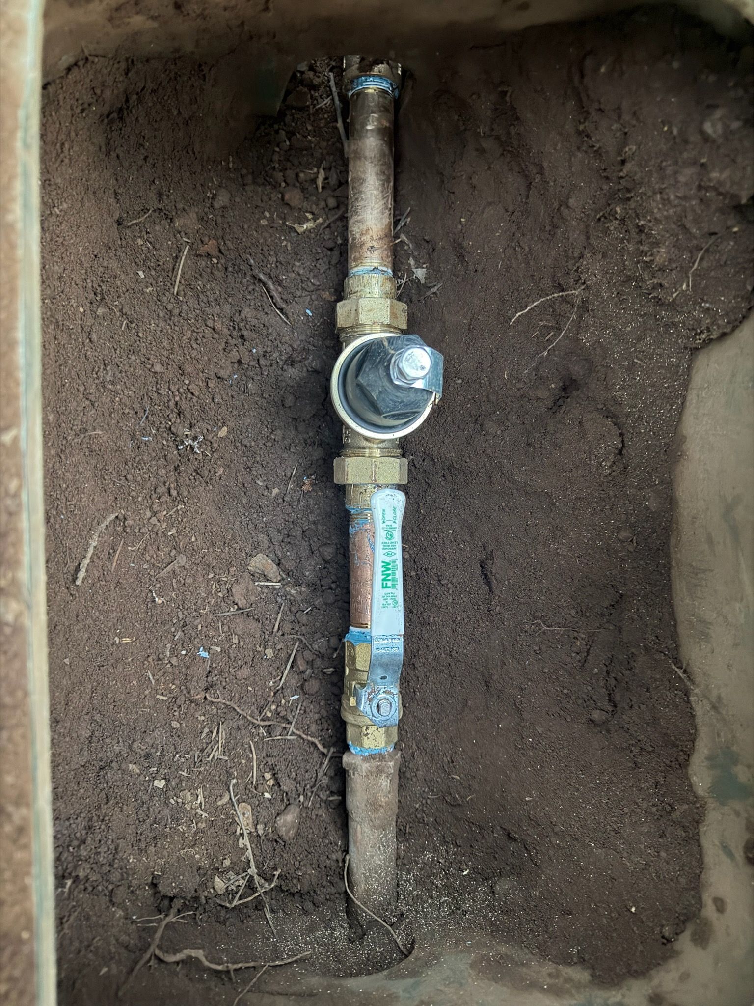 Metal irrigation valve assembly in a rectangular dirt-filled box.