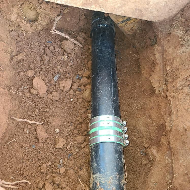 Black pipe section in earthen trench, clamped.