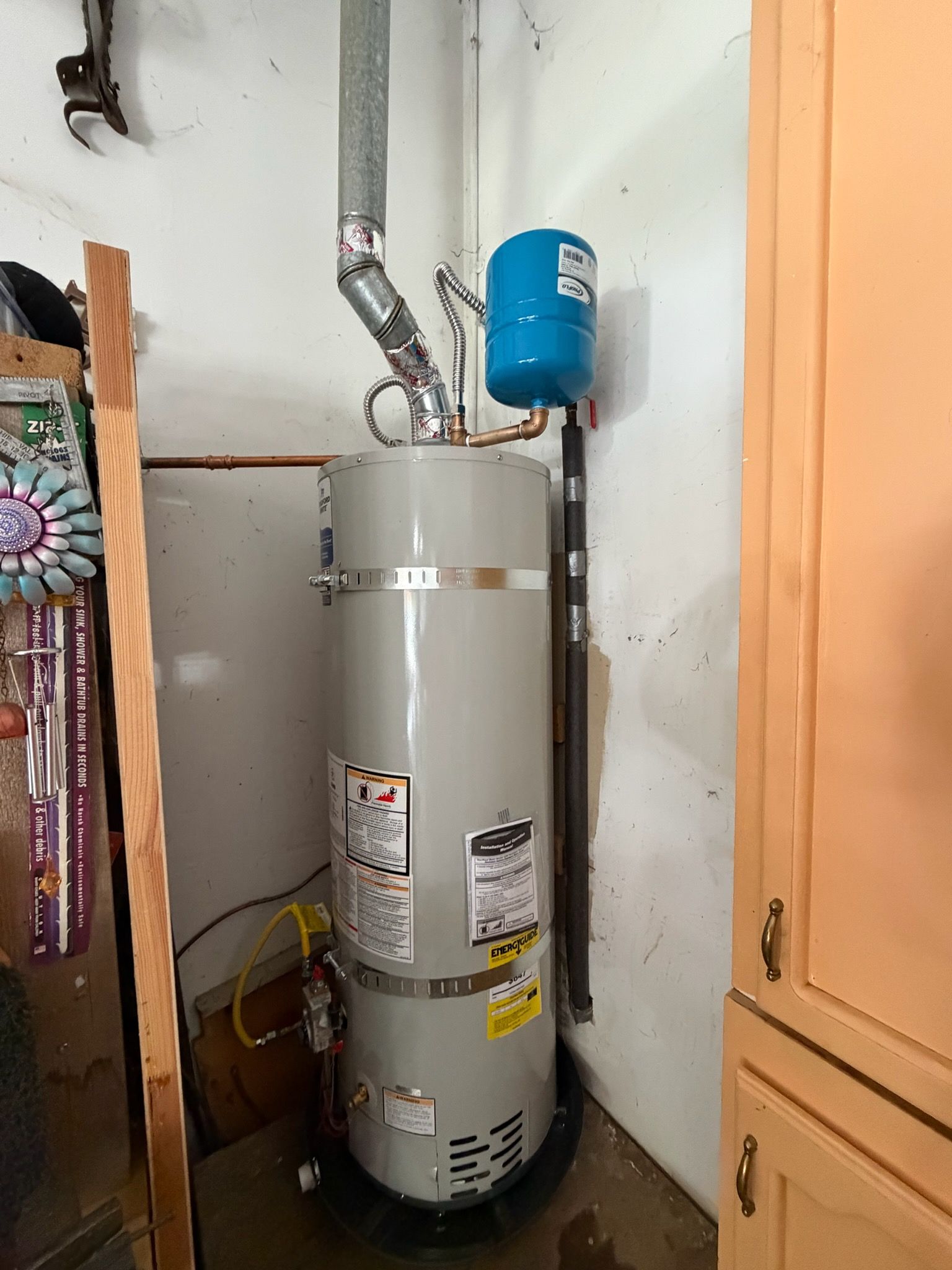 Gray water heater with blue expansion tank and exposed pipes in a closet corner