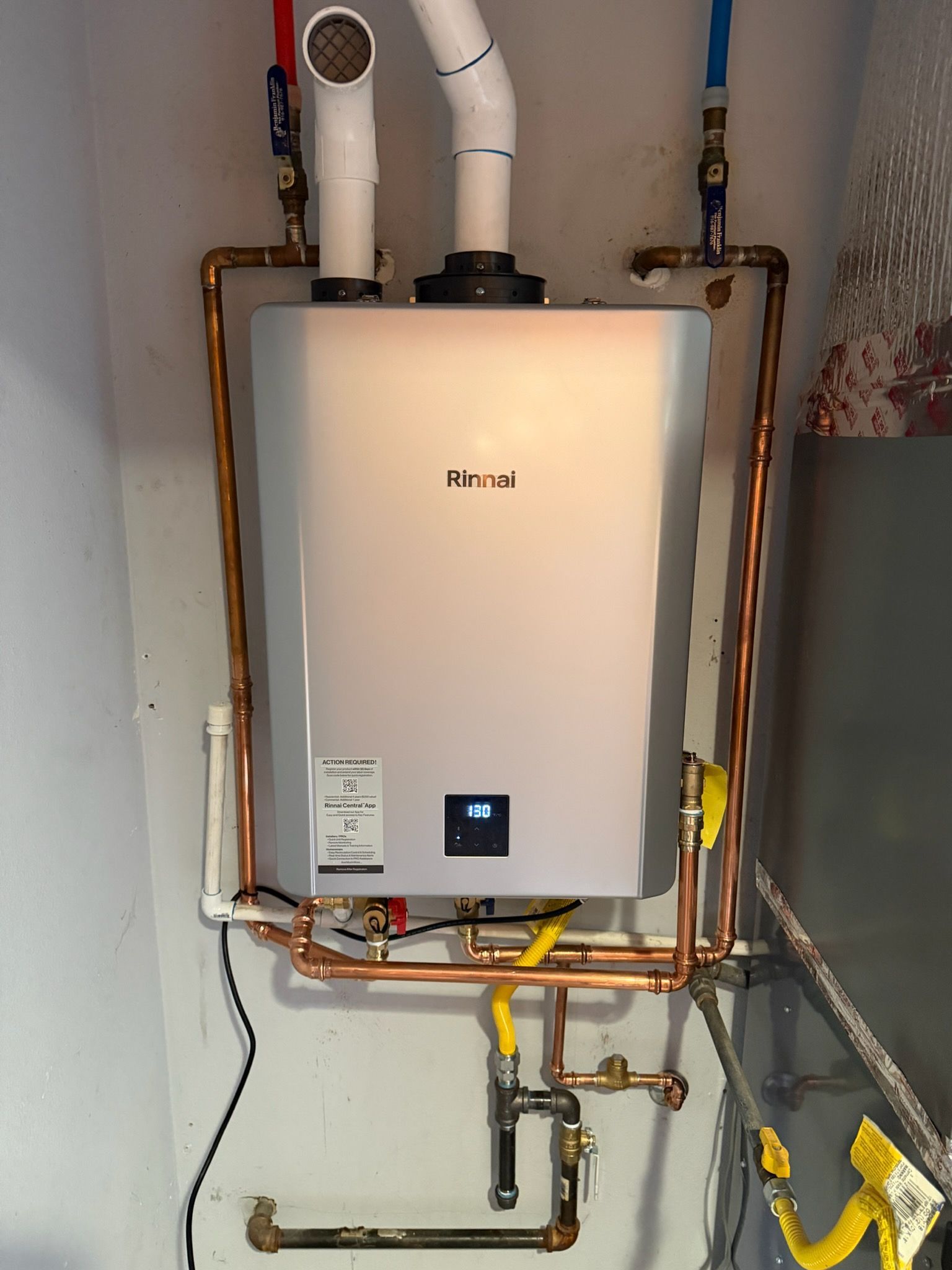 Wall-mounted Navien boiler with exposed copper pipes and vent pipes in a utility room.