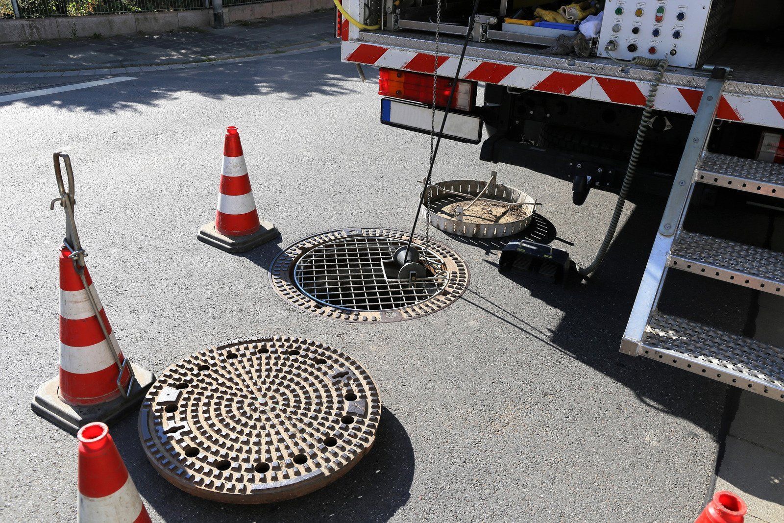 Road work site with open manhole, cones, and a utility truck, likely for sewer or utility maintenance.
