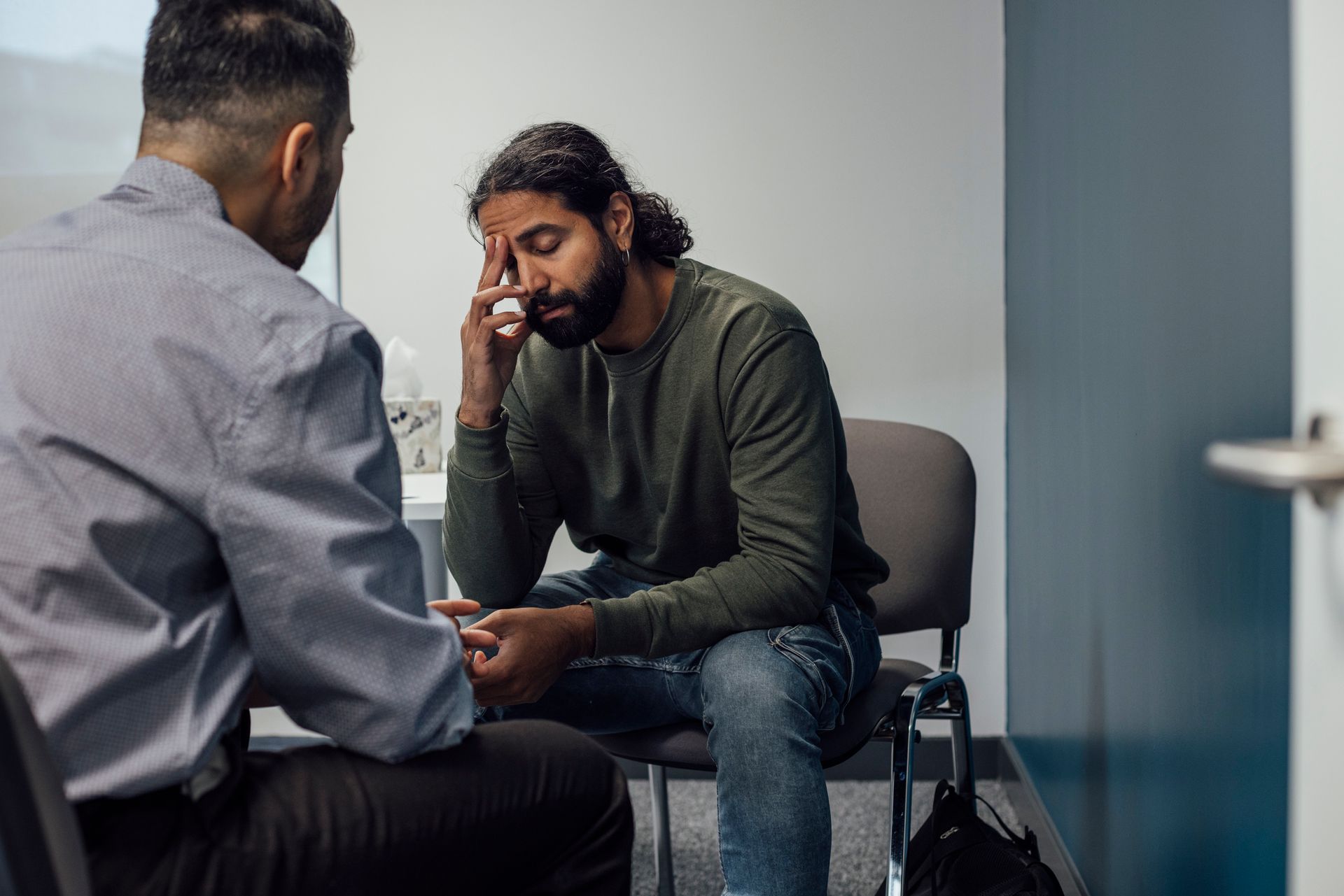 A man is sitting in a chair talking to another man.
