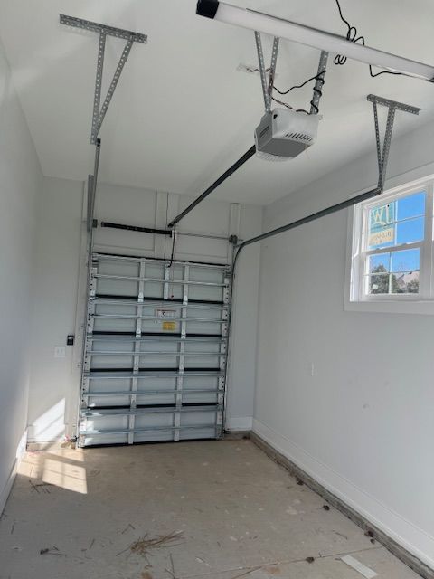 Empty garage with closed silver door, white walls, concrete floor, and window on right.