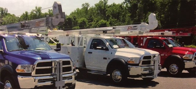 Three parked utility trucks in blue, white, and red with mounted boom lifts, positioned side-by-side outdoors.