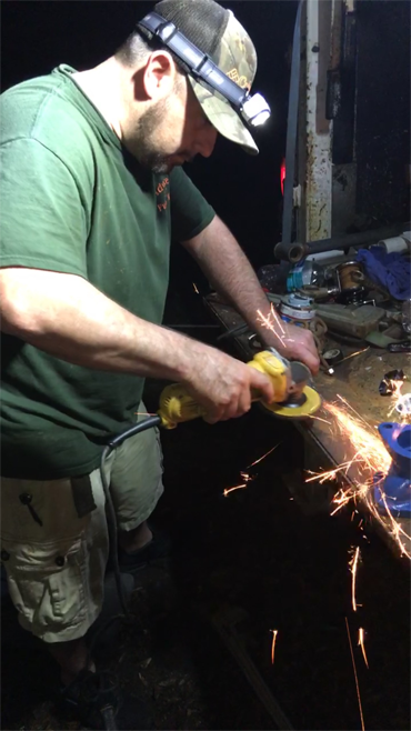 A person in a baseball cap with a headlamp uses an angle grinder to cut metal, creating a spray of sparks.