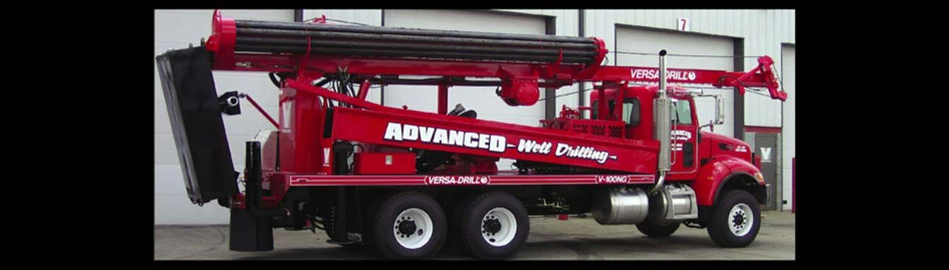 A red truck-mounted drilling rig parked in front of a white building.
