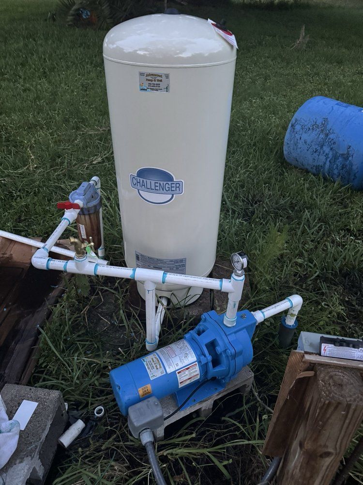 A blue water pump connected to a white pressurized water tank sitting outdoors on the grass.