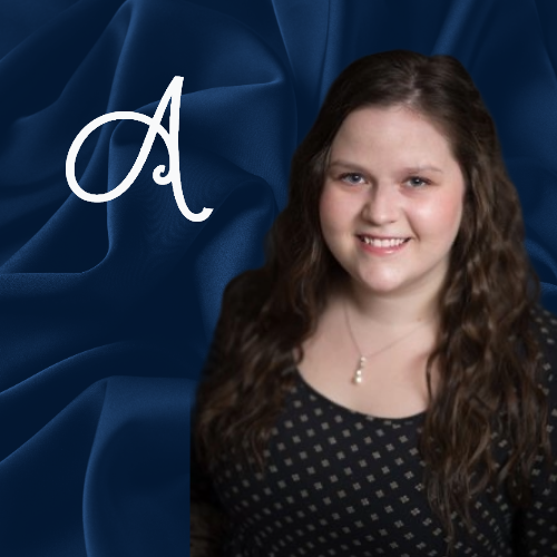 Portrait of a smiling woman in a dark top against a blue draped background with a white letter A