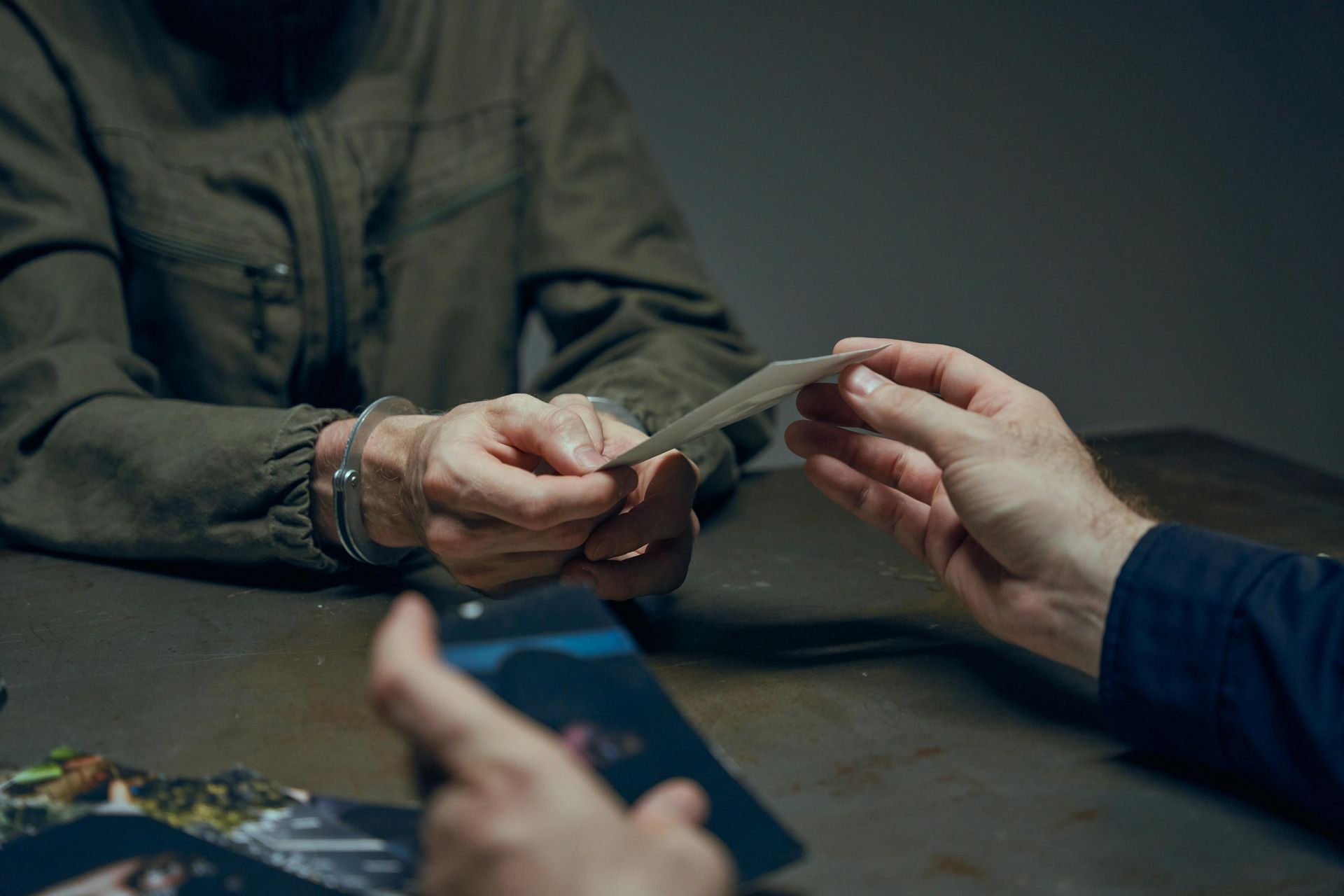 Hands exchanging paper money over a table, with one person holding a card and another using a phone