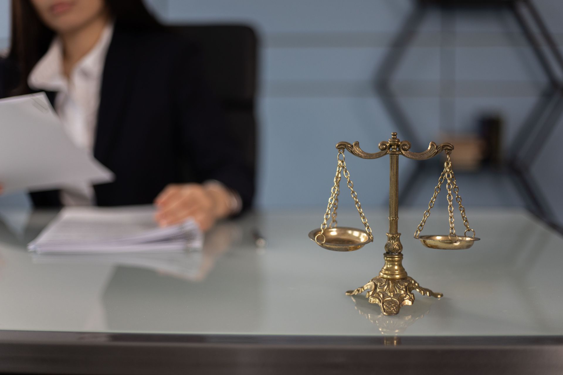 Law scales on a desk with an out-of-focus person reviewing documents in the background