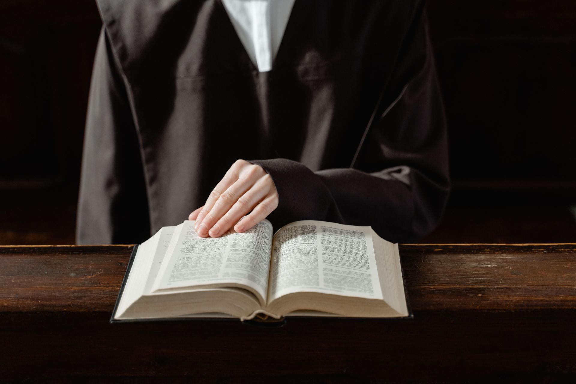 Person in black robe reading an open book at a wooden desk