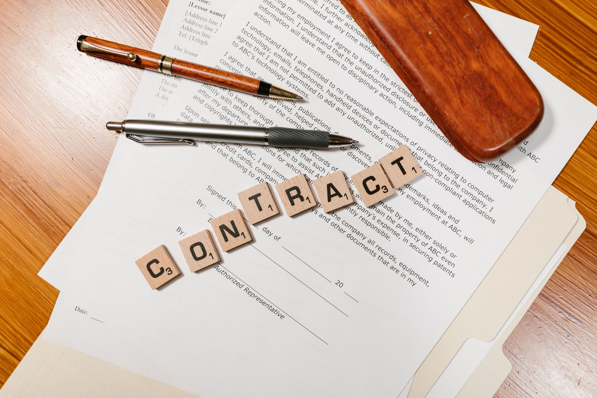Scrabble tiles spelling “CONTACT” on paperwork beside a pen and glasses on a wooden desk