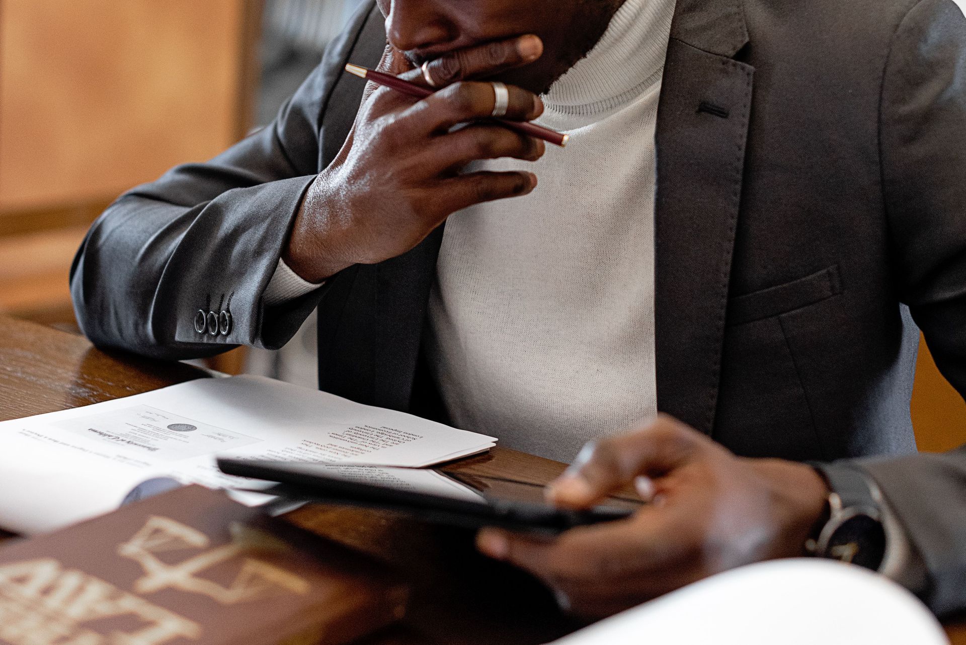 Person in a blazer using a phone at a desk with papers and a notebook nearby