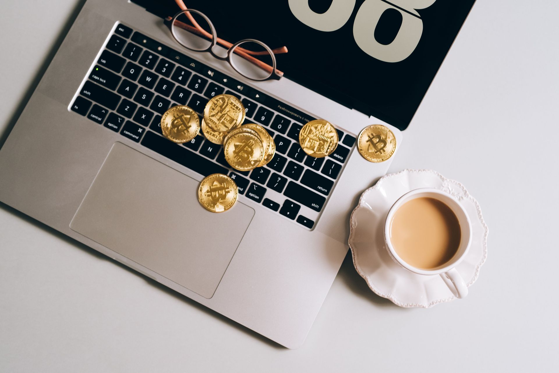 Laptop keyboard with gold coins and a cup of coffee on a desk