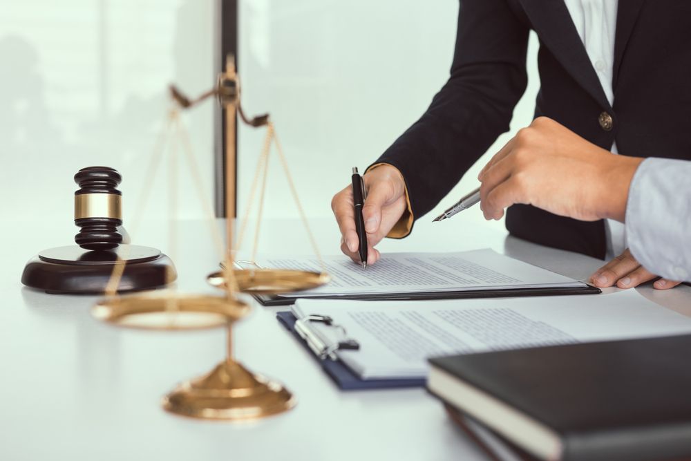 Lawyer signing documents at desk with scales and gavel in a courtroom office