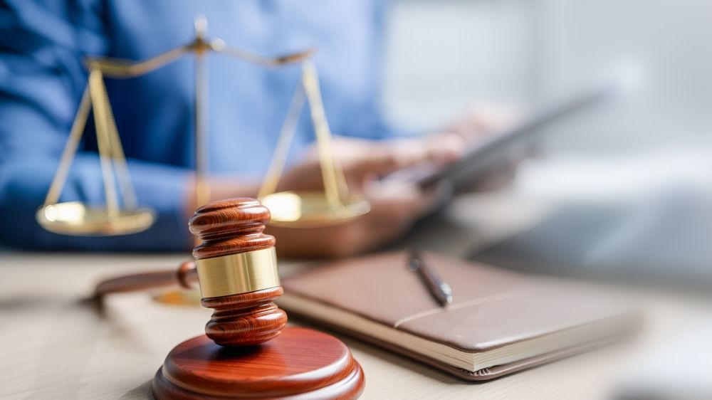 Legal scales and a judge’s gavel on a desk with a notebook, in a courtroom-themed setting