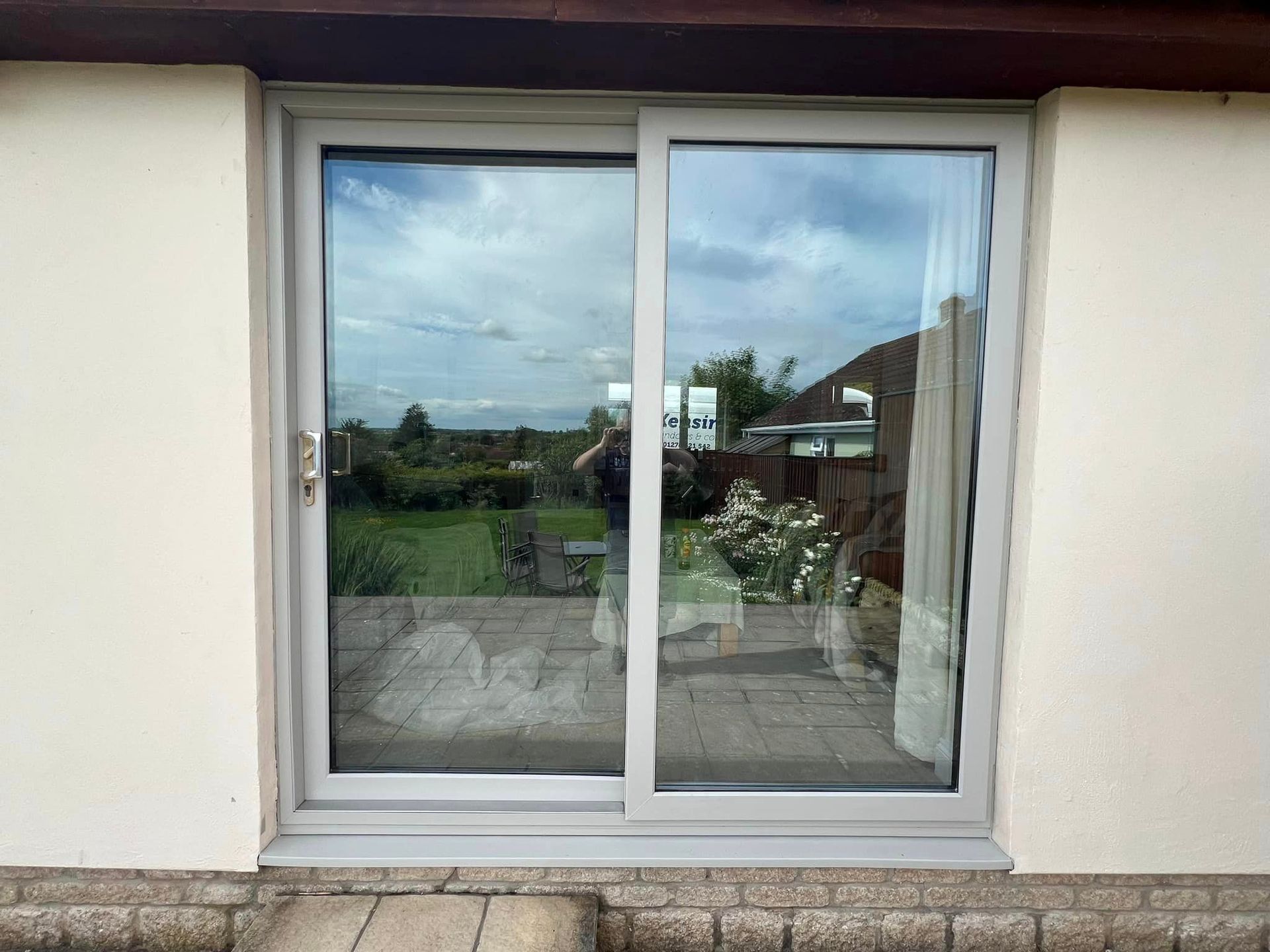 A white sliding glass door with a reflection of a person in the window.