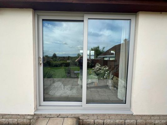 A white sliding glass door with a reflection of a person in the window.