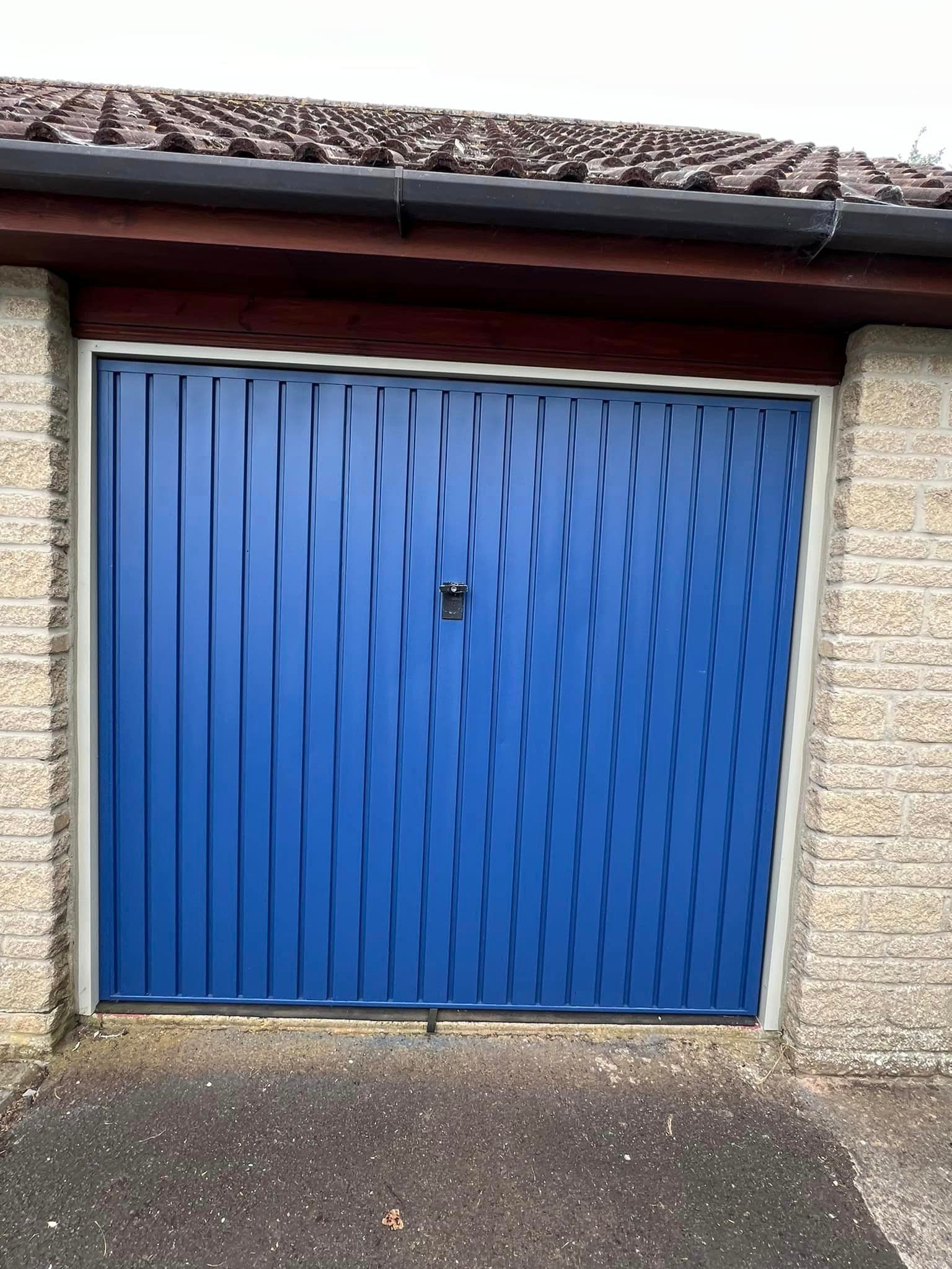 A blue garage door is sitting in front of a brick building.