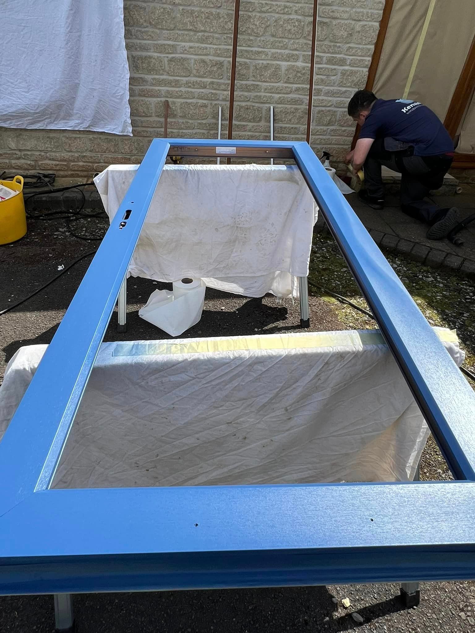 A man is working on a blue door frame outside