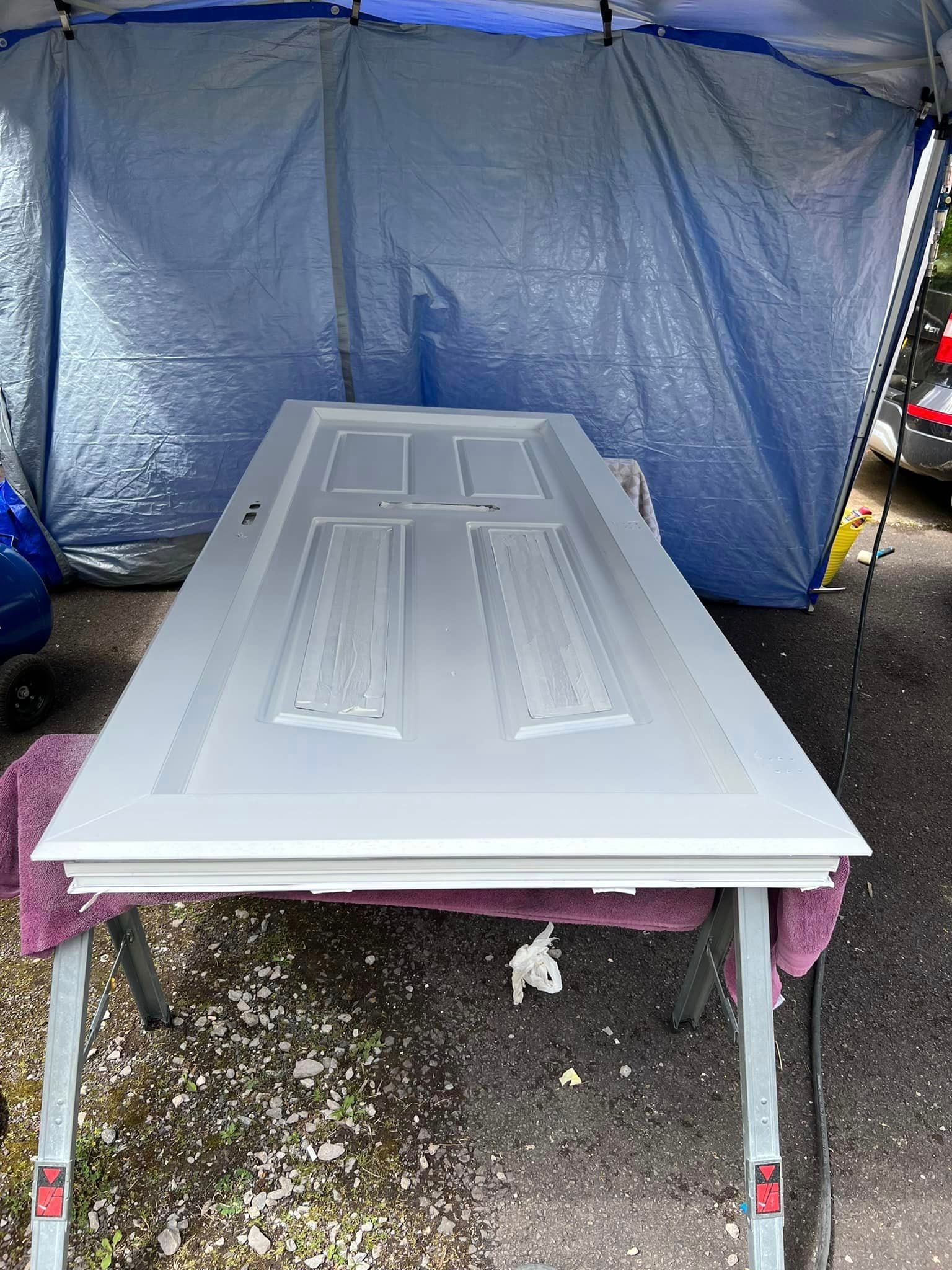 A white door is sitting on a table in front of a blue tarp.