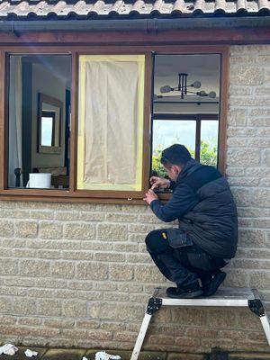 A man is kneeling on a ladder working on a window.