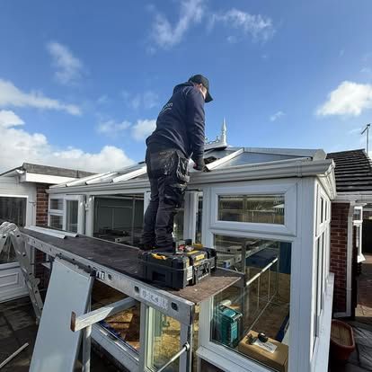 Worker standing on a ladder installing solar panels on a house roof under a blue sky