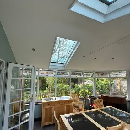 Bright sunroom with skylights, white walls, glass doors, and wooden tables overlooking a garden