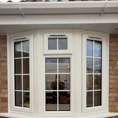 White bay window with three panes under a house eave, with a person reflected in the center glass