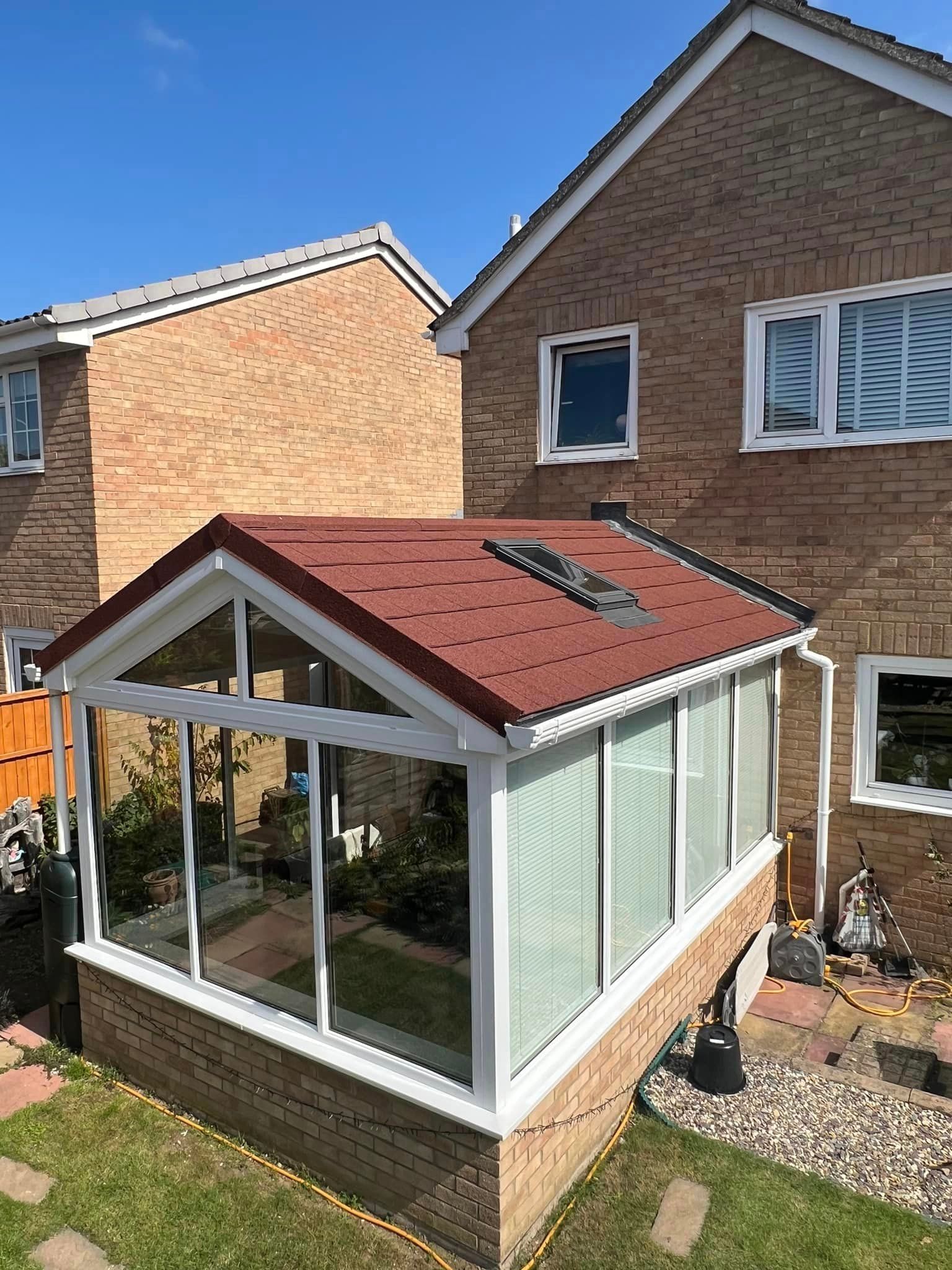 Small white sunroom with red roof beside a brick house in a backyard