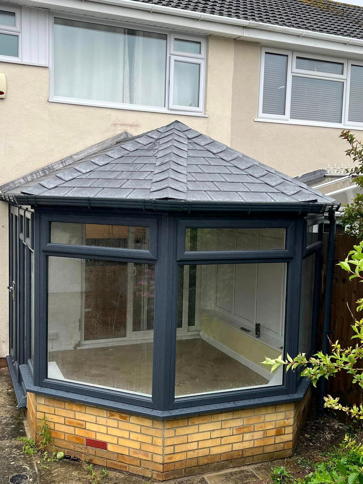 A conservatory with a slate roof is sitting in front of a house.