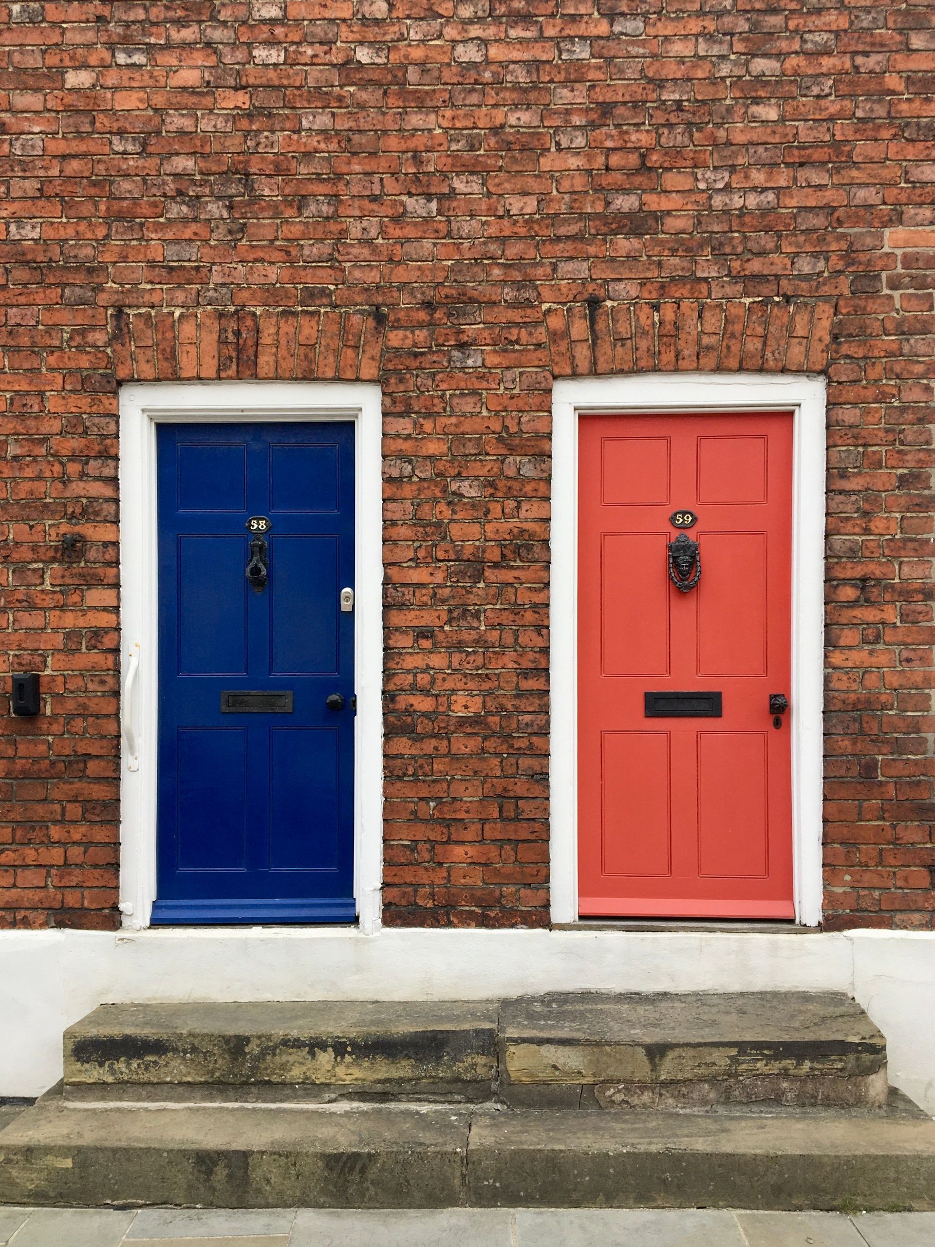 Two colorful front doors, blue and coral, set in a brick wall above stone steps