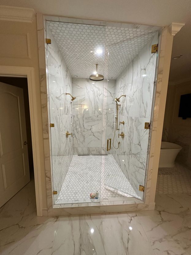 Glass-enclosed shower with white marble walls and floor, gold fixtures, and a glass door.